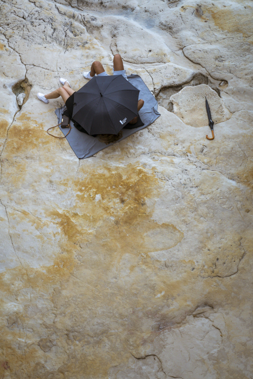 Un couple d'amoureux allongé sur les rochers se cache derrière son parapluie.
