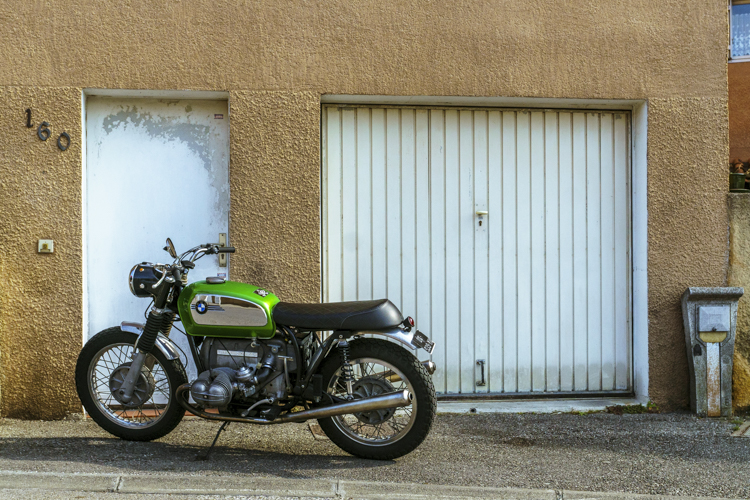 Une moto BMW des années soixante-dix rutilante et fièrement garée devant un garage.