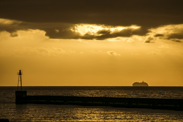 Un ferry sur la ligne d'horizon part au soleil couchant vers des contrées lontaines.