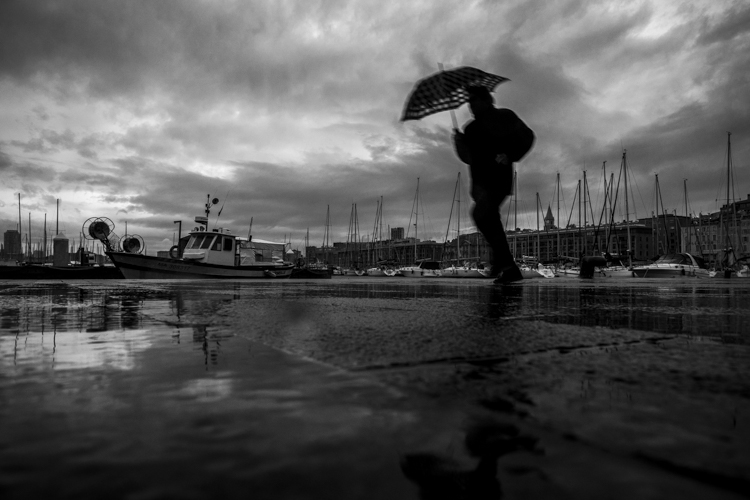 Un homme � l'abri de son parapluie presse le pas sur le Vieux-Port de Marseille, sous un ciel charg� de nuages et une pluie battante.