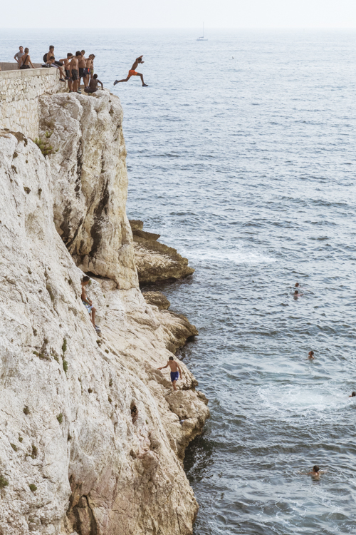 Un groupe d'adolescents sur les hauteurs de la Corniche Président John Fitzgerald Kennedy à Marseille s'élancent tour à tour pour sauter dans la Méditerranée une dizaine de mètre plus bas.