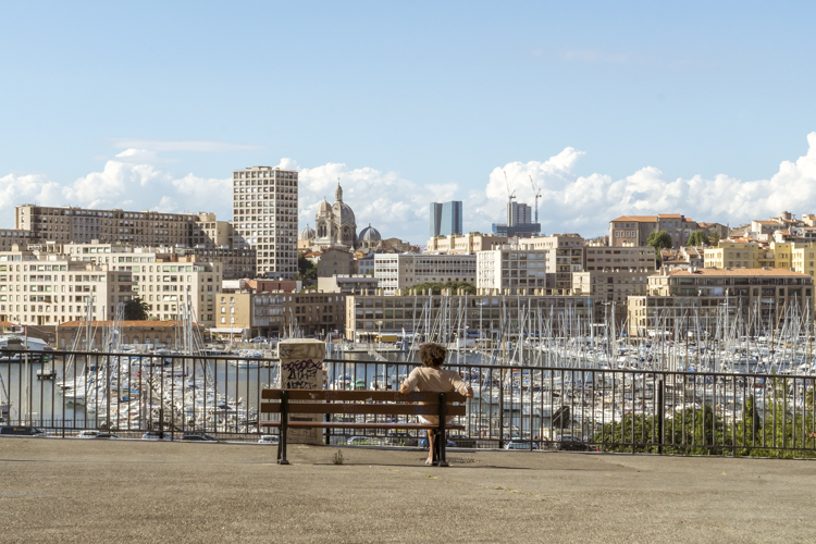 Une femme assise sur un banc contemple les vieux-port de Marseille.