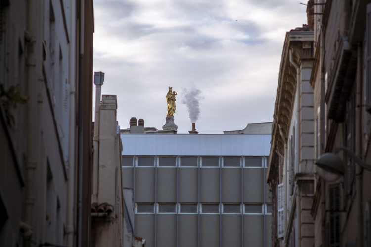 Depuis la rue du Petit Chantier dans le 7ème arrondissement de Marseille, par-dessus les toits dépasse juste la statue en or qui orne Notre Dame de la Garde.