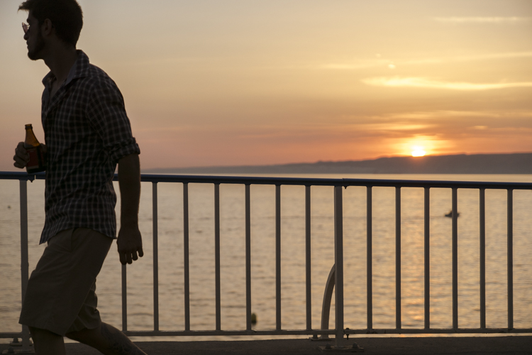 Un homme marche le long de la corniche à Marseille au soleil couchant et une bière à la main.