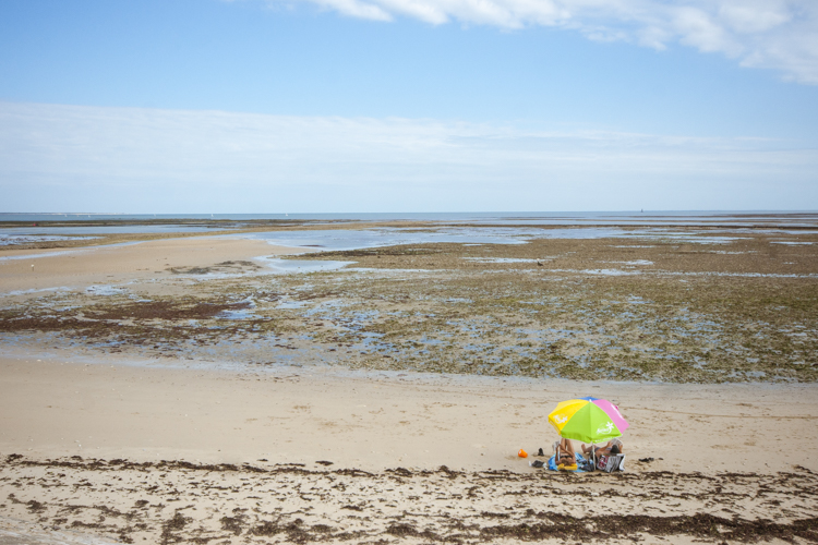 Sur une plage complétement désertique de l'Ile de Ré, un couple est installé sous son parasol.
