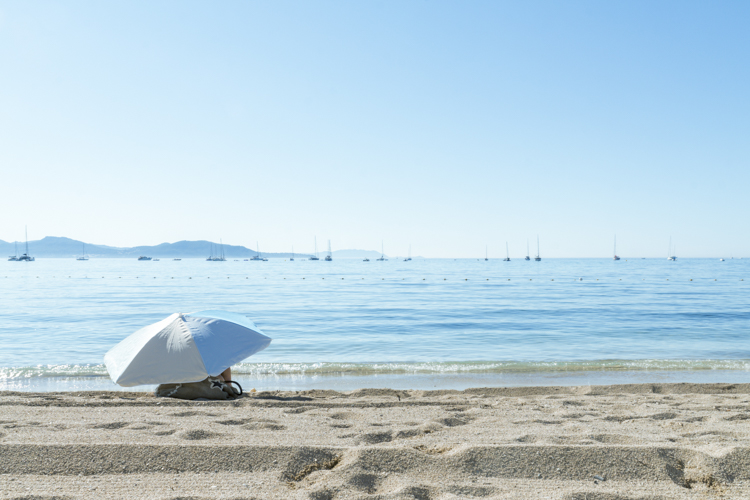 Par une matinée d'été, un parasol blanc et bleu est seul sur la plage.