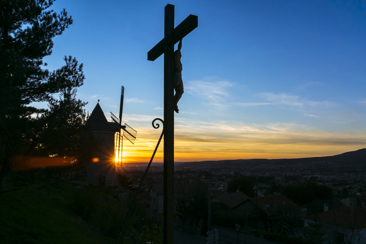 Le Christ sur sa croix au pied des moulins du village d'Allauch sous le soleil couchant.