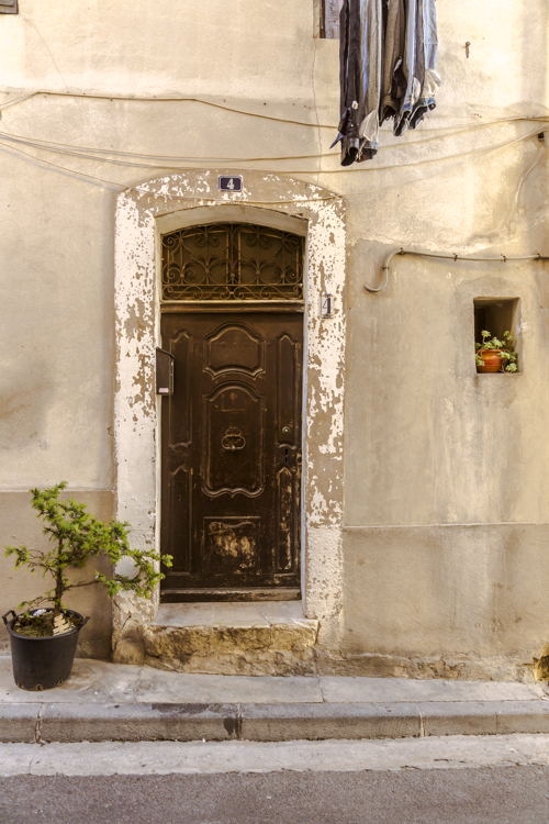 Une porte d'entrée, une plante en pot sur le côté et du linge qui pend dans une rue du village d'Allauch.