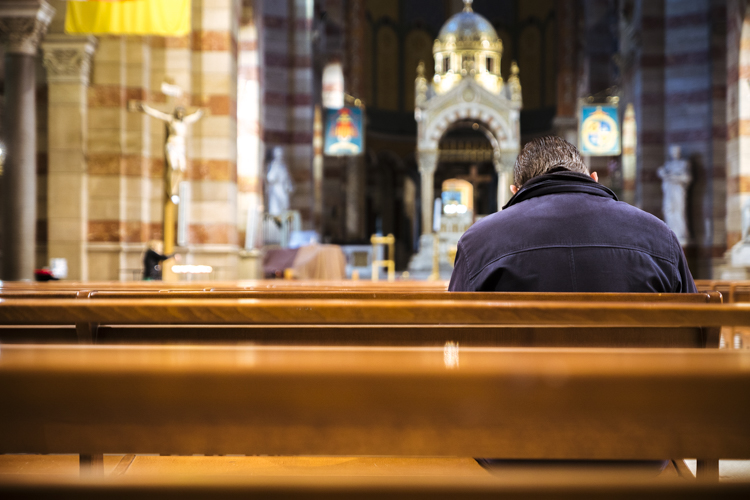 Un homme assis, la tête baissée, seul dans la cathédrale de la Major à Marseille prie